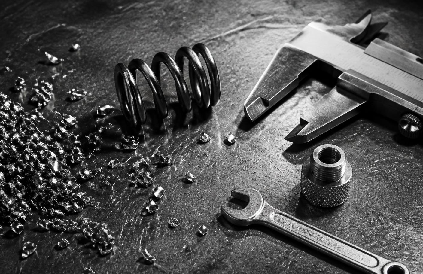 Machinist bench with brass shavings, a steel spring, calipers and a knurled fitting